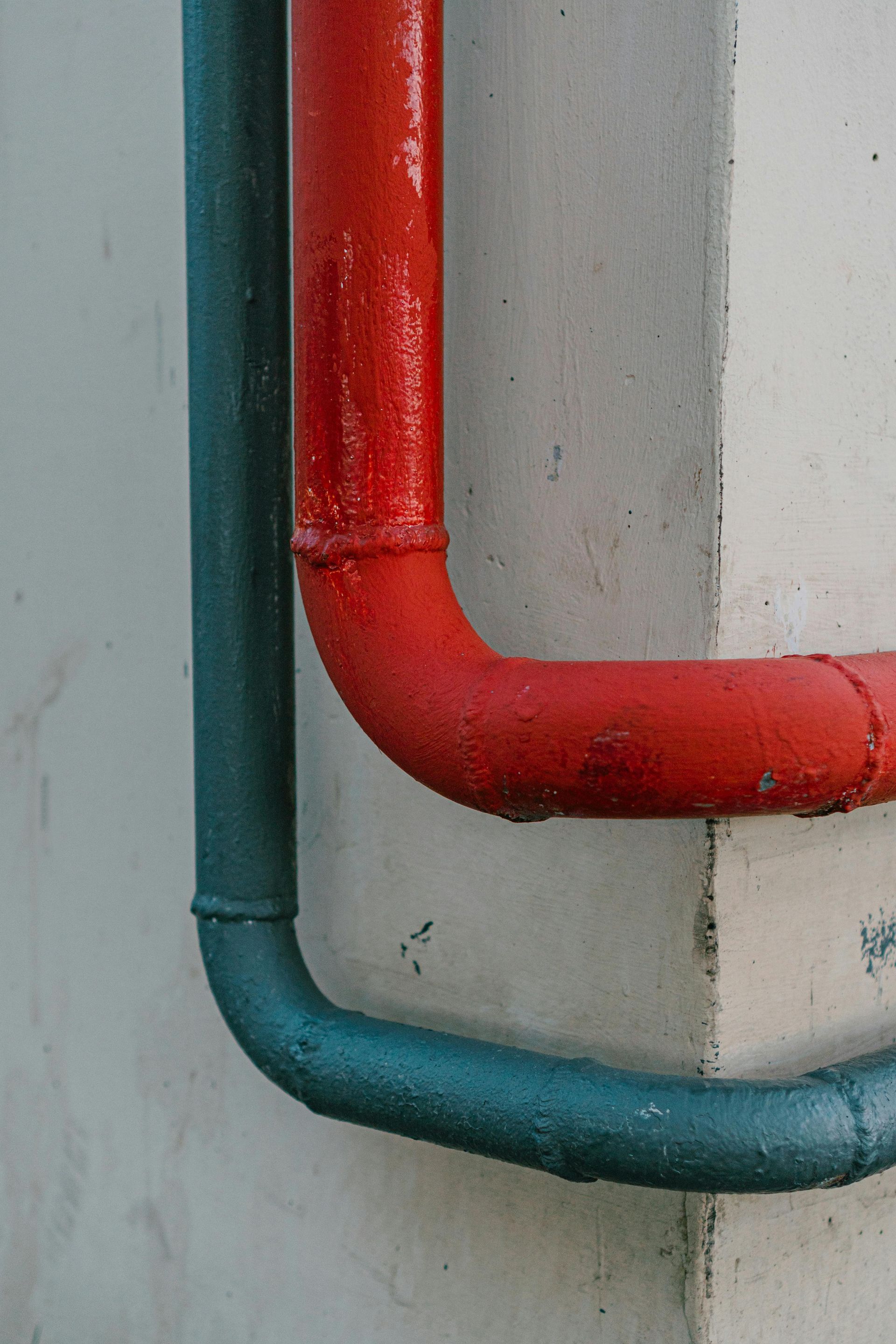 Red and blue painted pipes run along a white concrete wall.