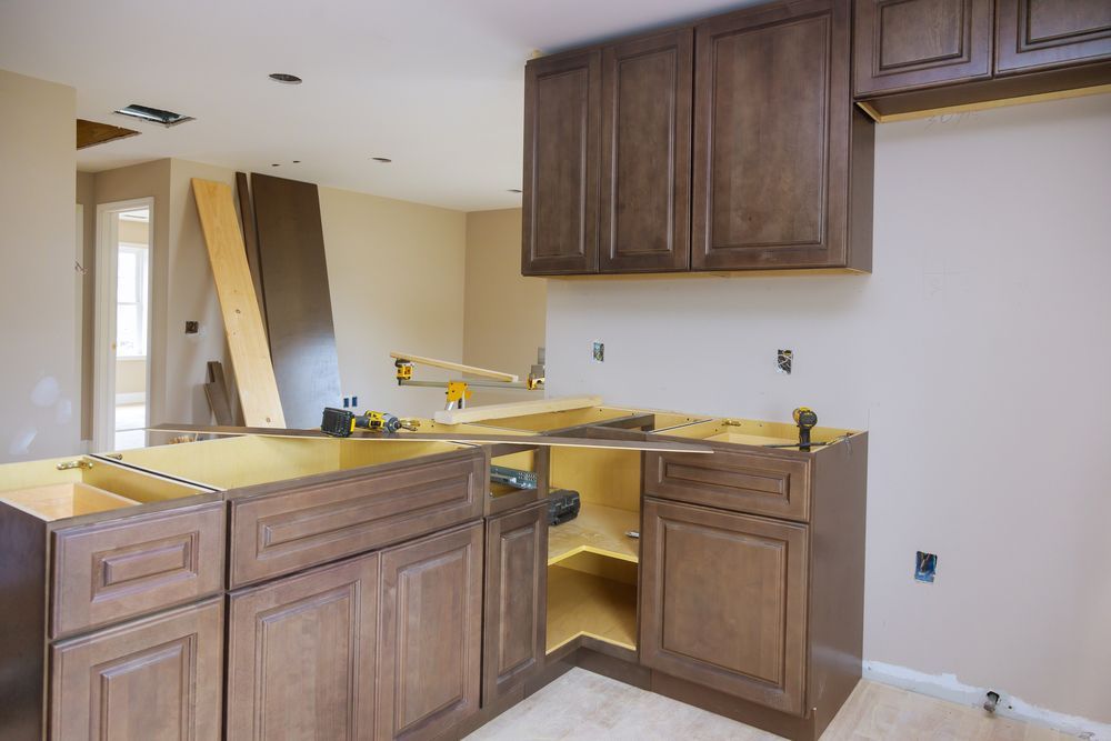Partially renovated kitchen with unfinished wood cabinets, yellow countertop covers, and open wall space
