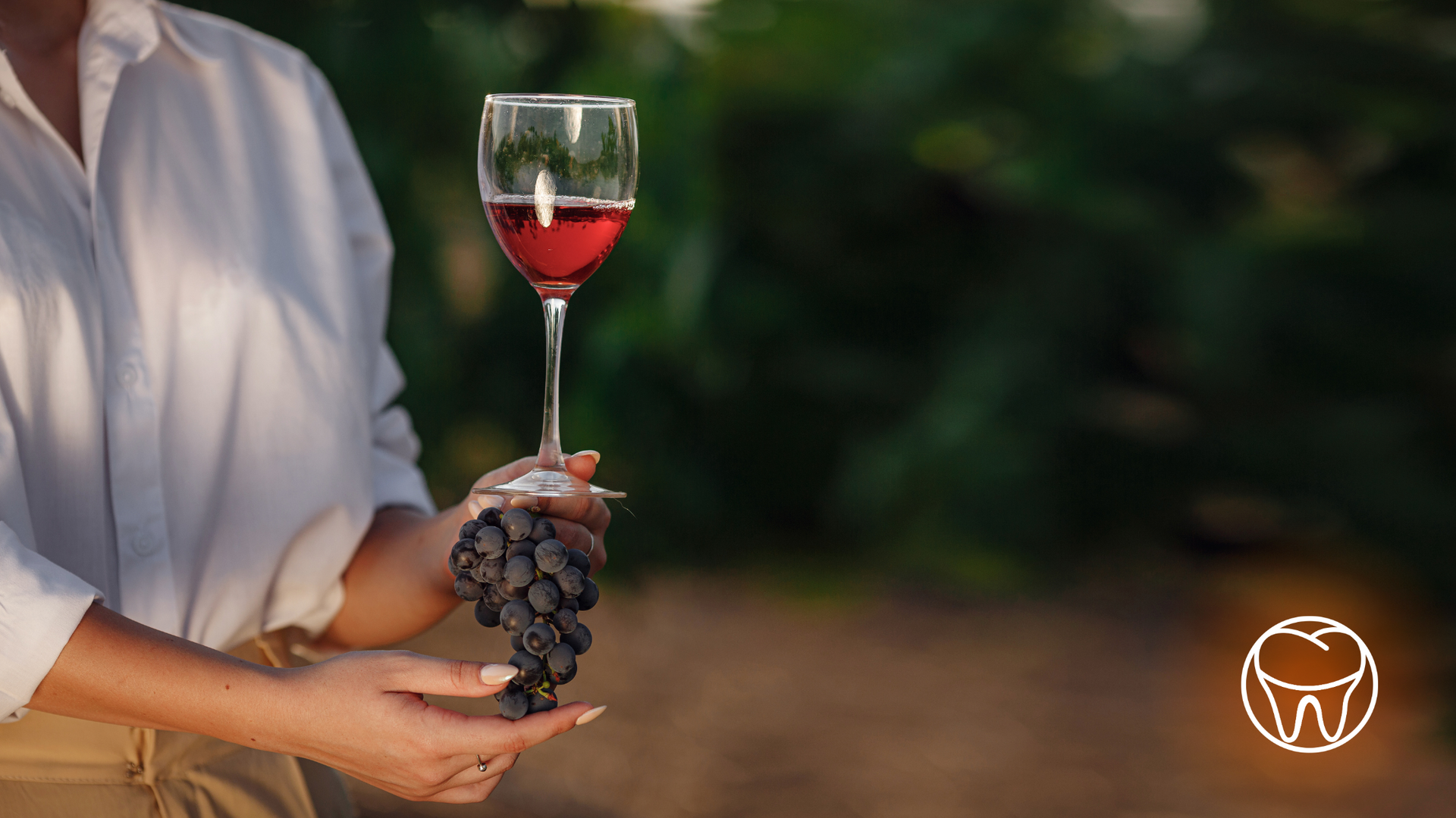 A woman is holding a bunch of grapes and a glass of wine.