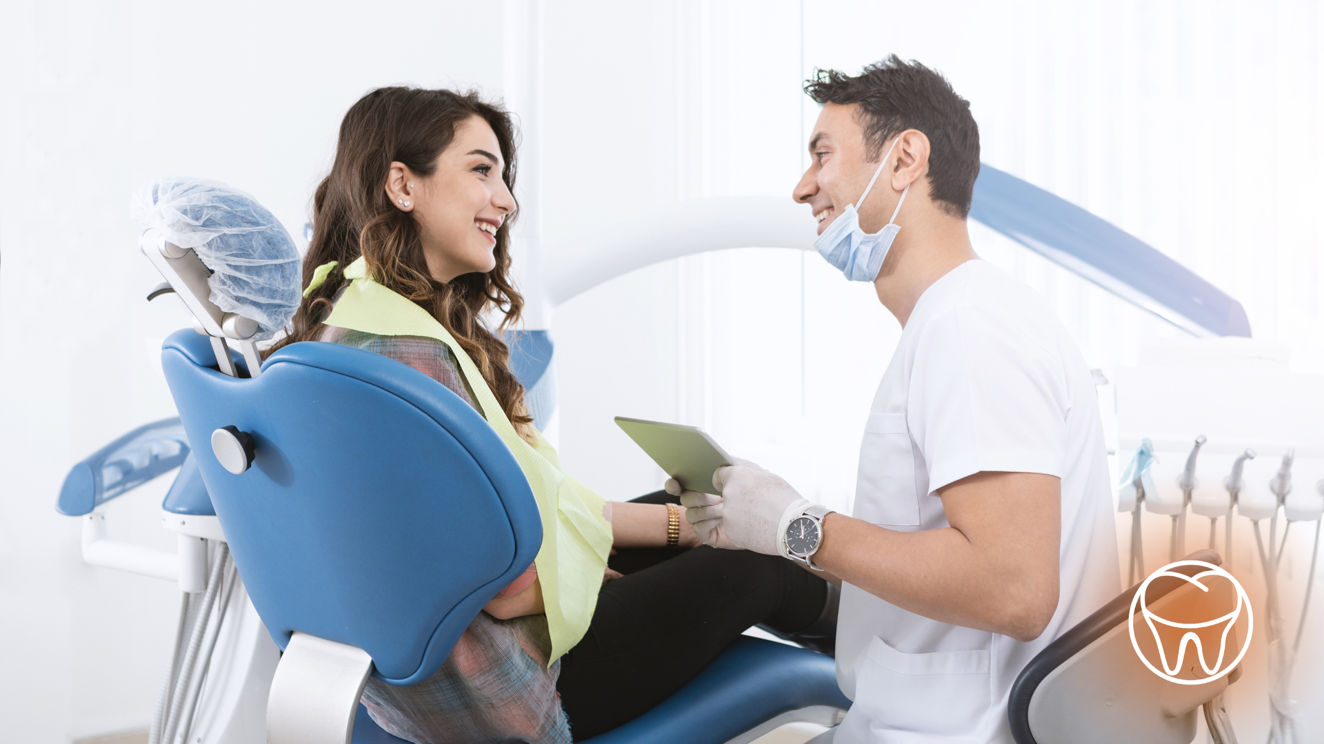 Woman in dental chair smiles at dentist holding tablet; bright office setting.