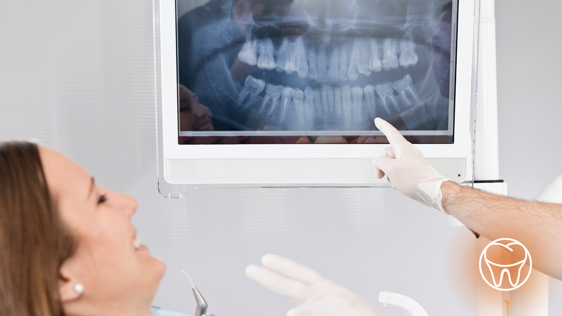 A woman is sitting in a dental chair looking at an x-ray of her teeth.
