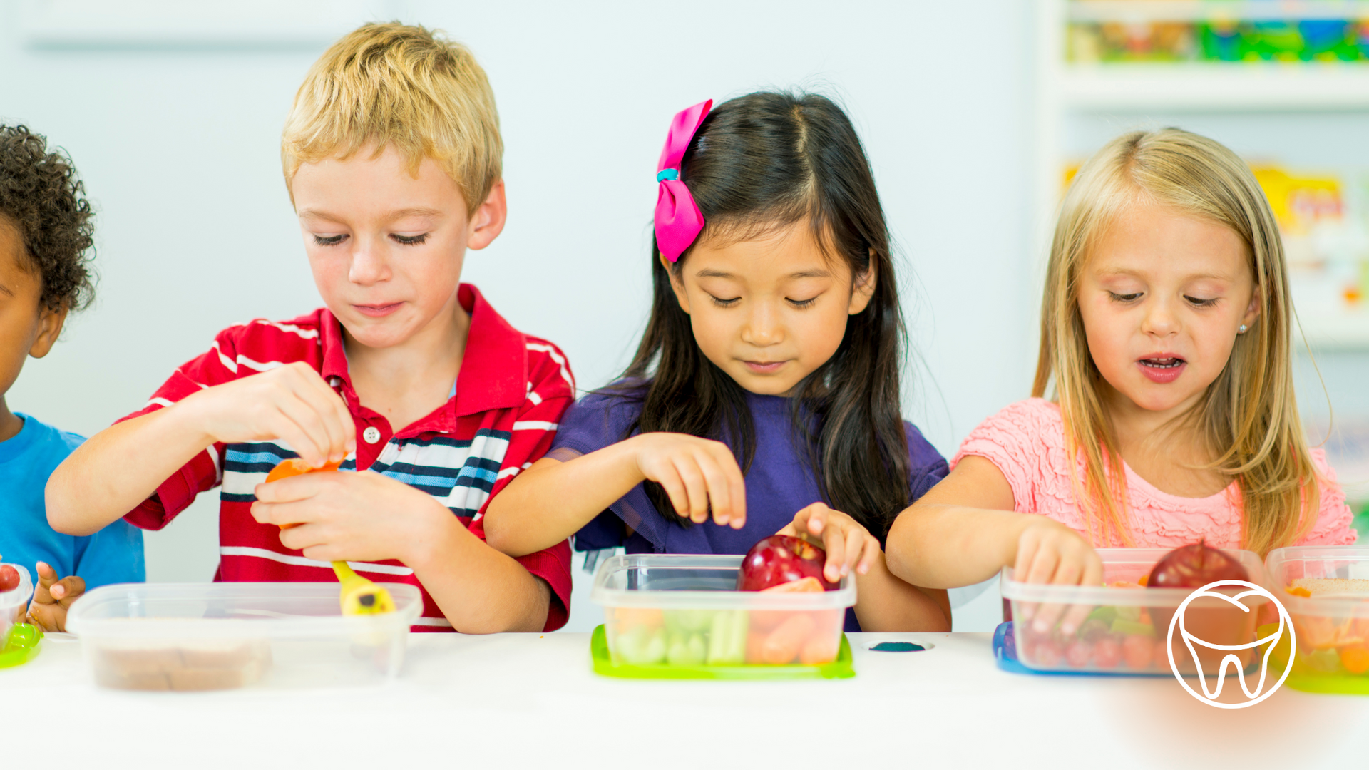 Children at a table preparing lunch with fruit and other food.