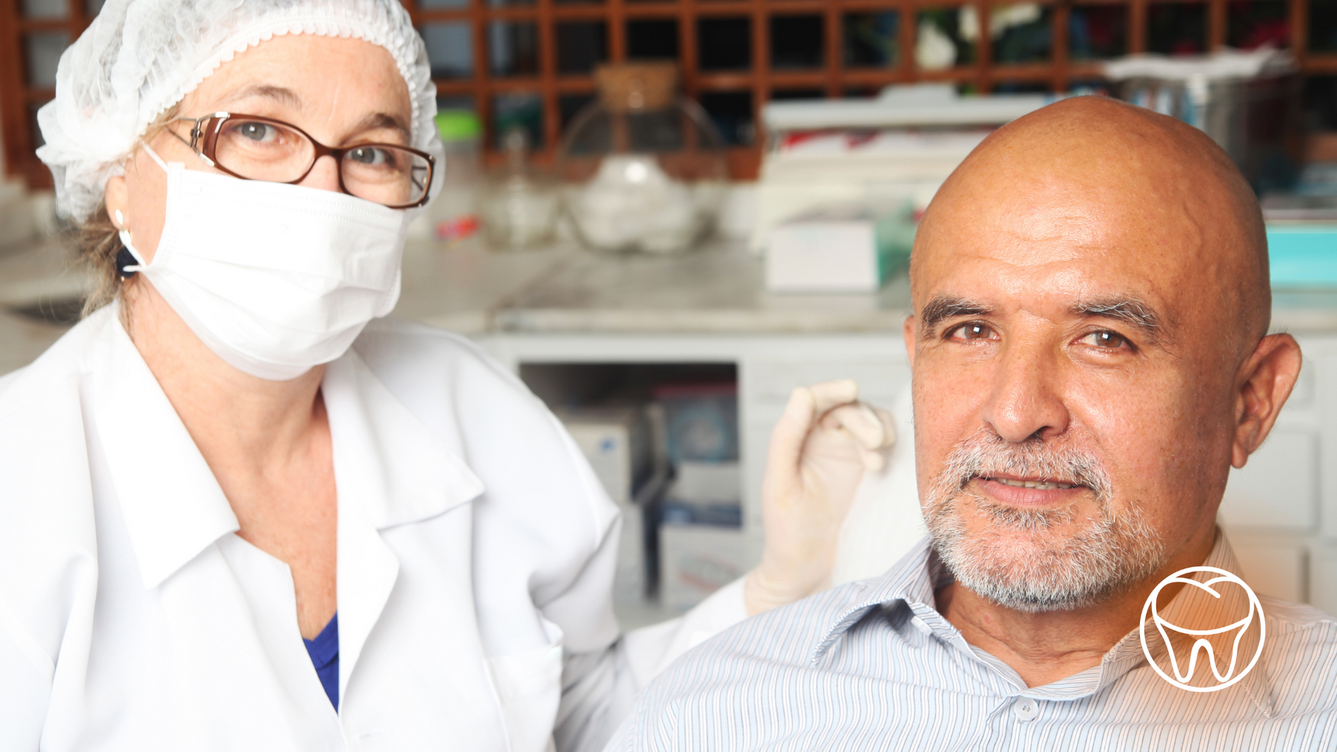 A man is sitting in a dental chair next to a woman wearing a mask.