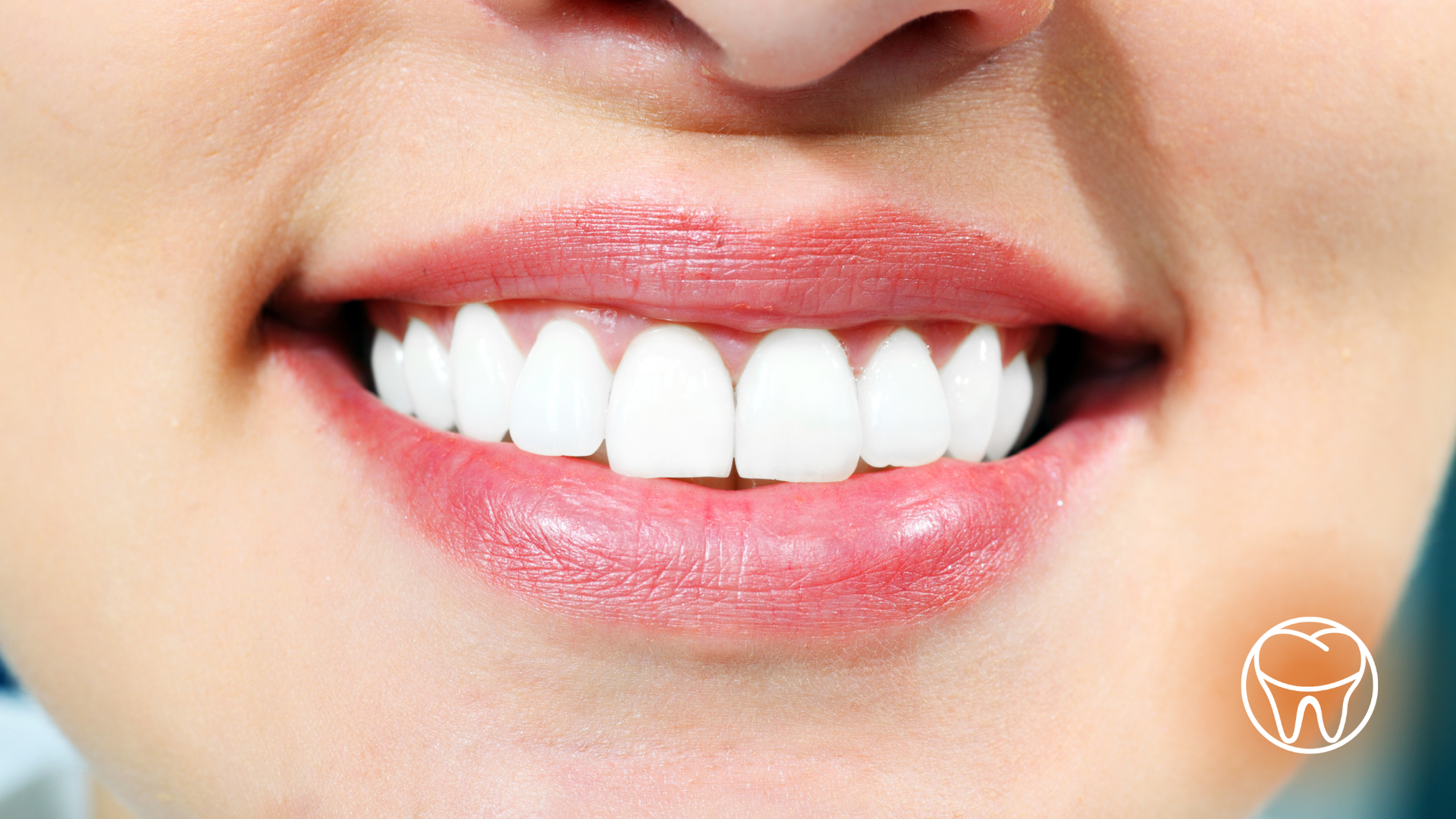 Close-up of a smiling mouth with white teeth and full, glossy pink lips.