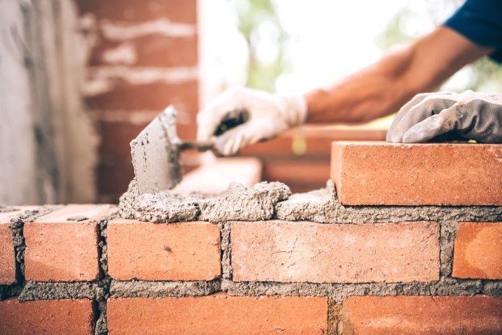 Mason laying bricks on a brick wall with mortar and a trowel outdoors
