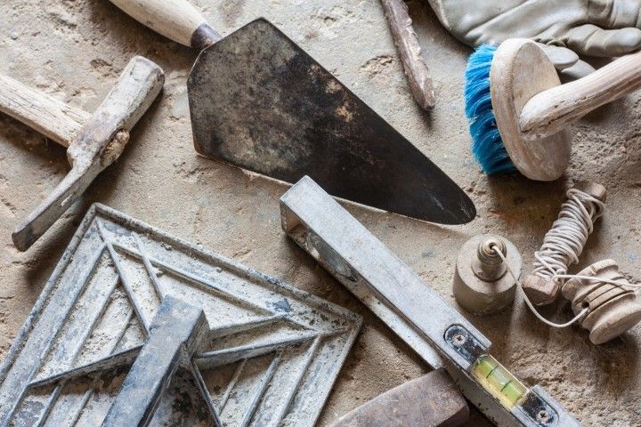 Dusty construction tools on a work surface, including a trowel, level, brush, and tile spacers