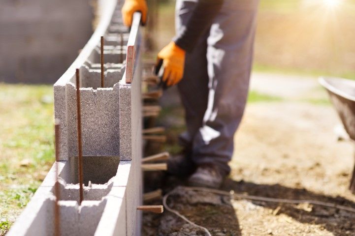 Construction worker laying concrete blocks along a foundation wall outdoors