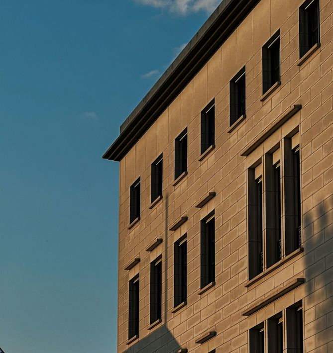 Sunlit tan brick building facade with tall windows against a blue sky