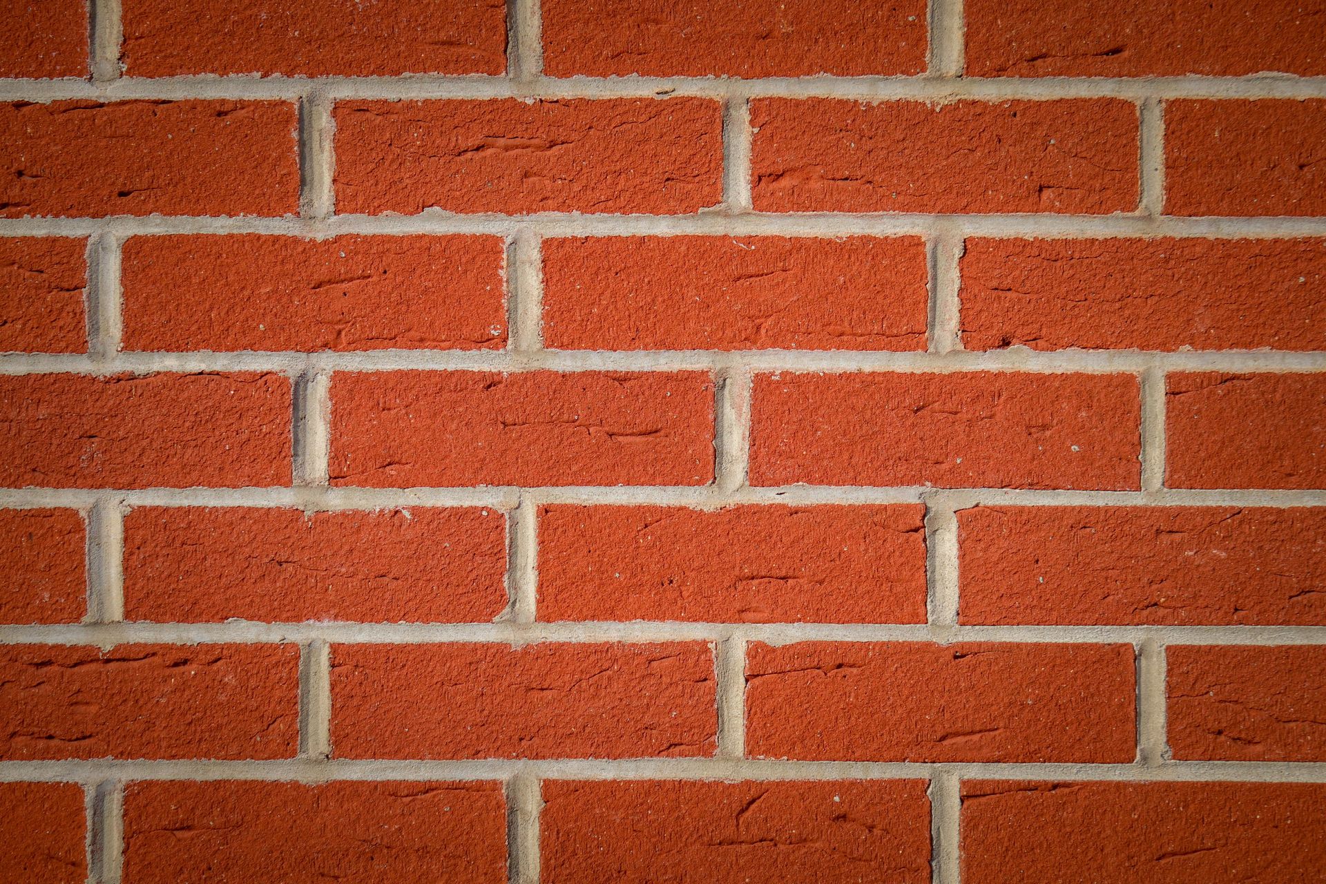 Red brick wall with horizontal mortar lines and a few small stains