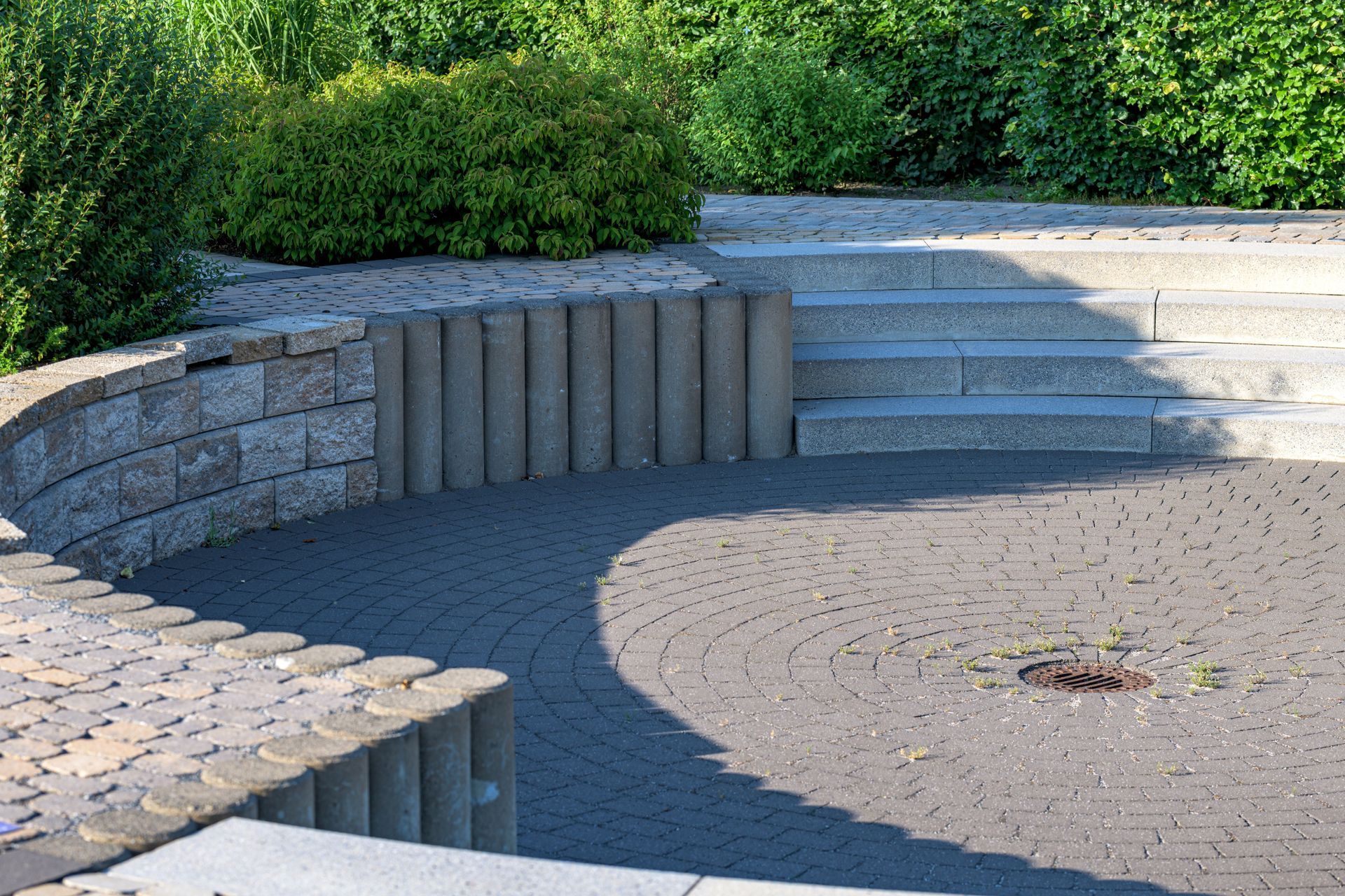 Curved stone seating around a circular paved courtyard with stairs and green hedges nearby