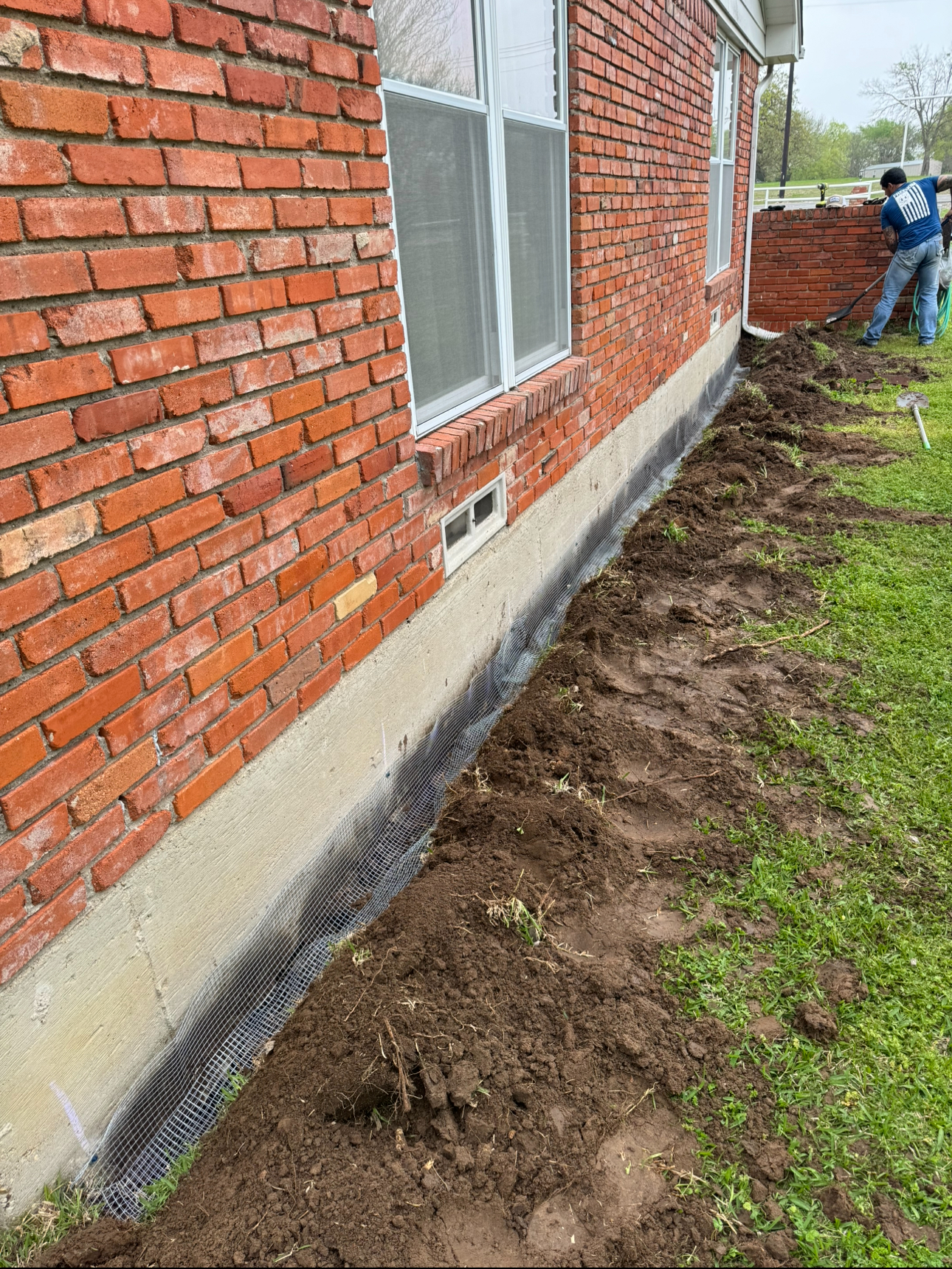 Brick building with gravel along the foundation, dirt, and grass. Person in background.