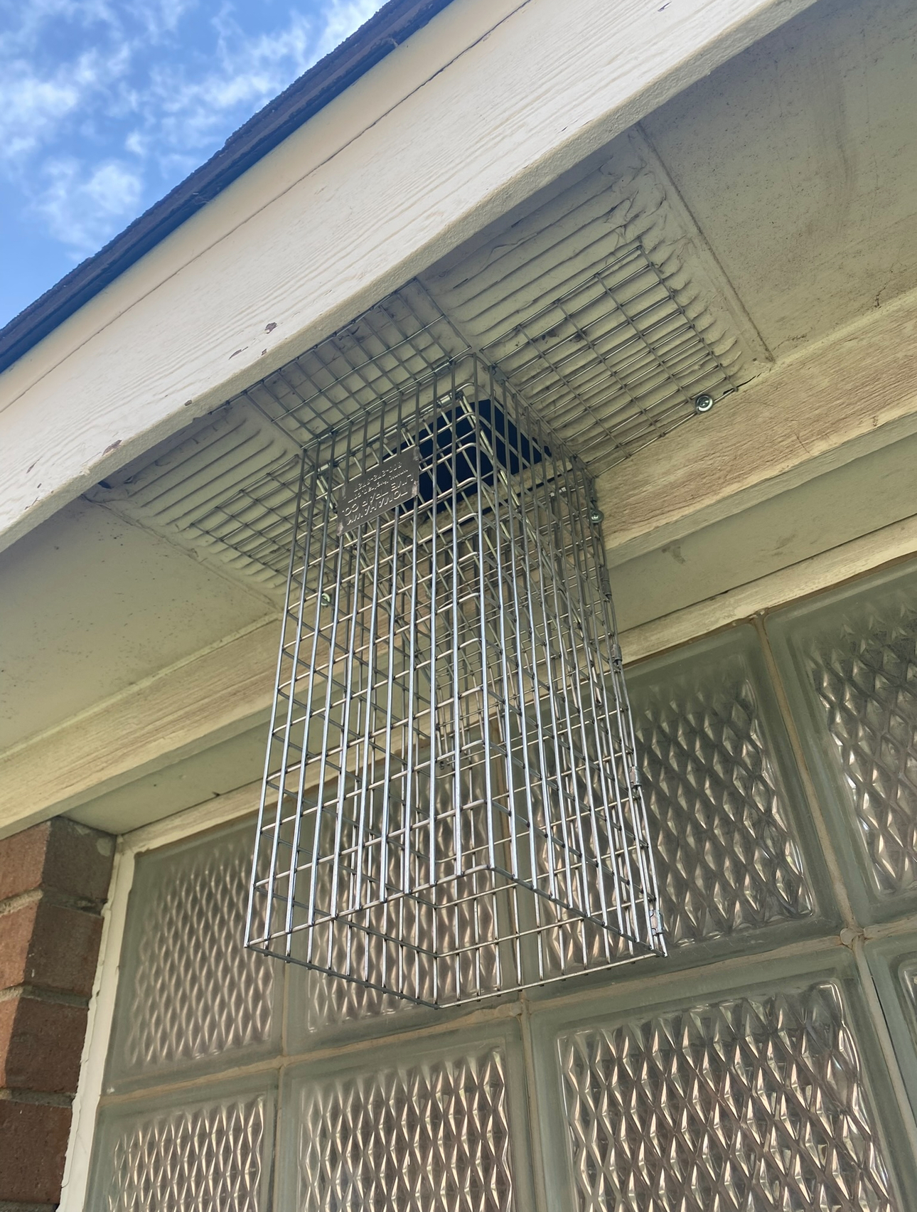 Metal cage protecting a vent on a building's exterior, above a window.