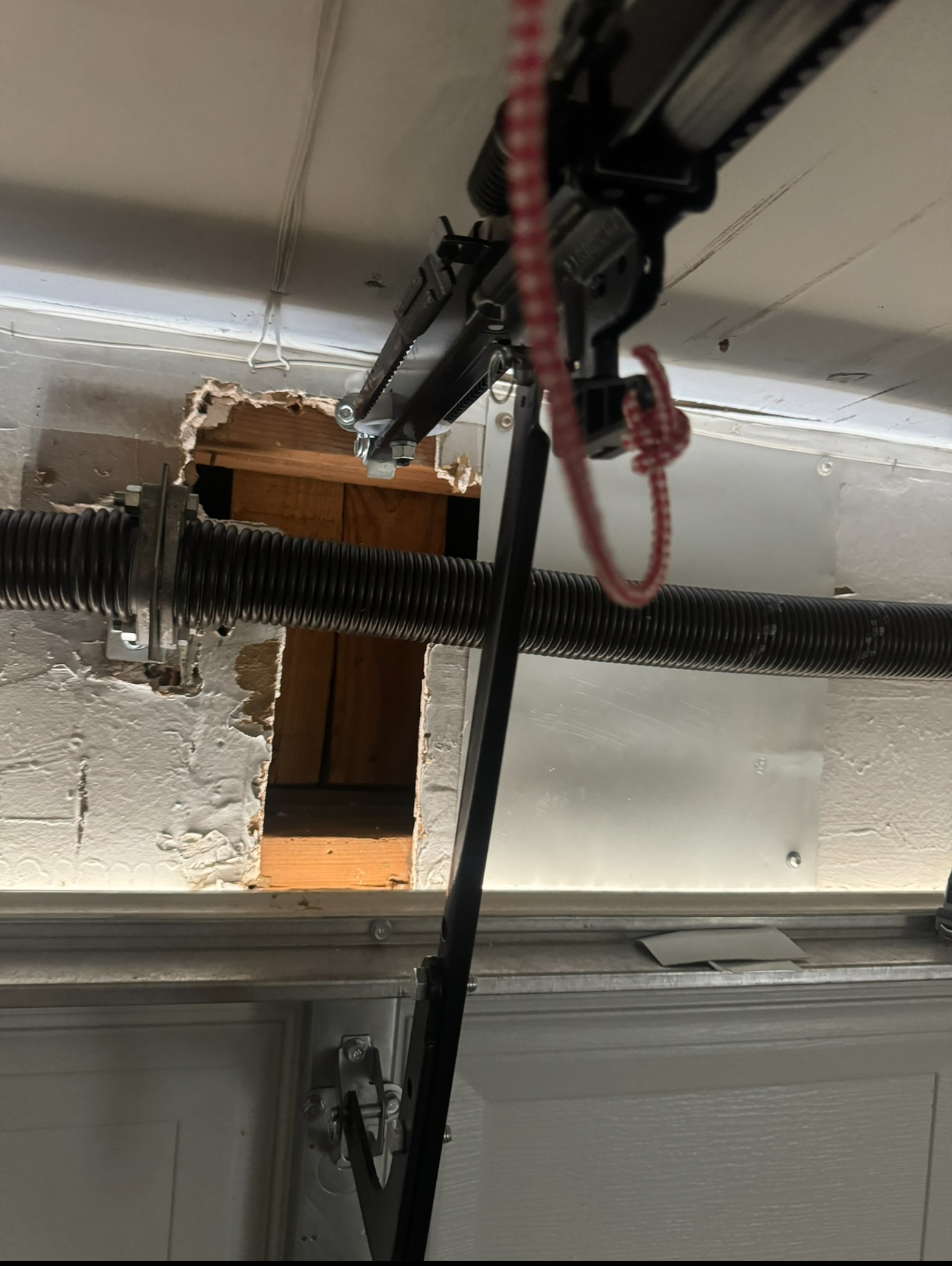 Garage door opener hardware damaged, hole in wall exposing wood, springs, and door arm.