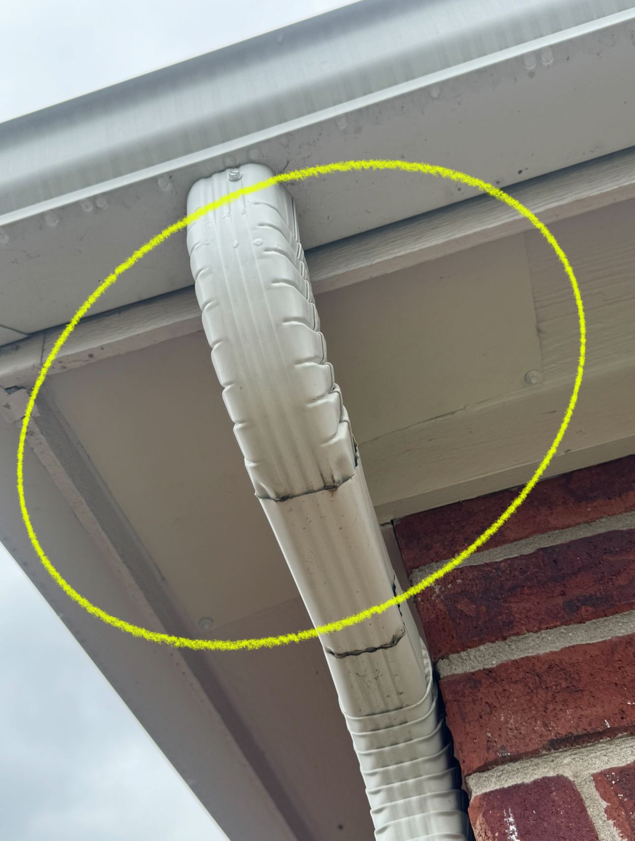 White gutter elbow attached to a white soffit on a brick building, circled in yellow.
