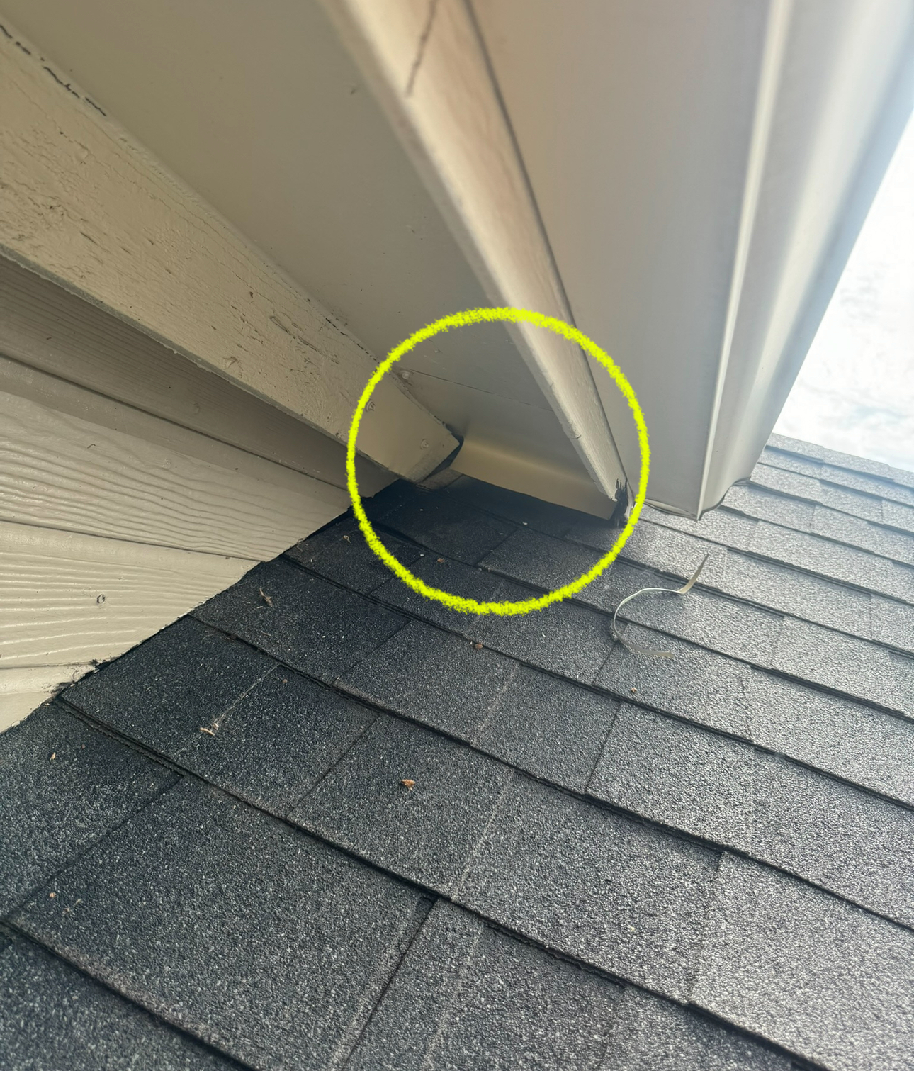 Yellow circle highlights a gap between roof and soffit on a beige house with dark gray shingles.