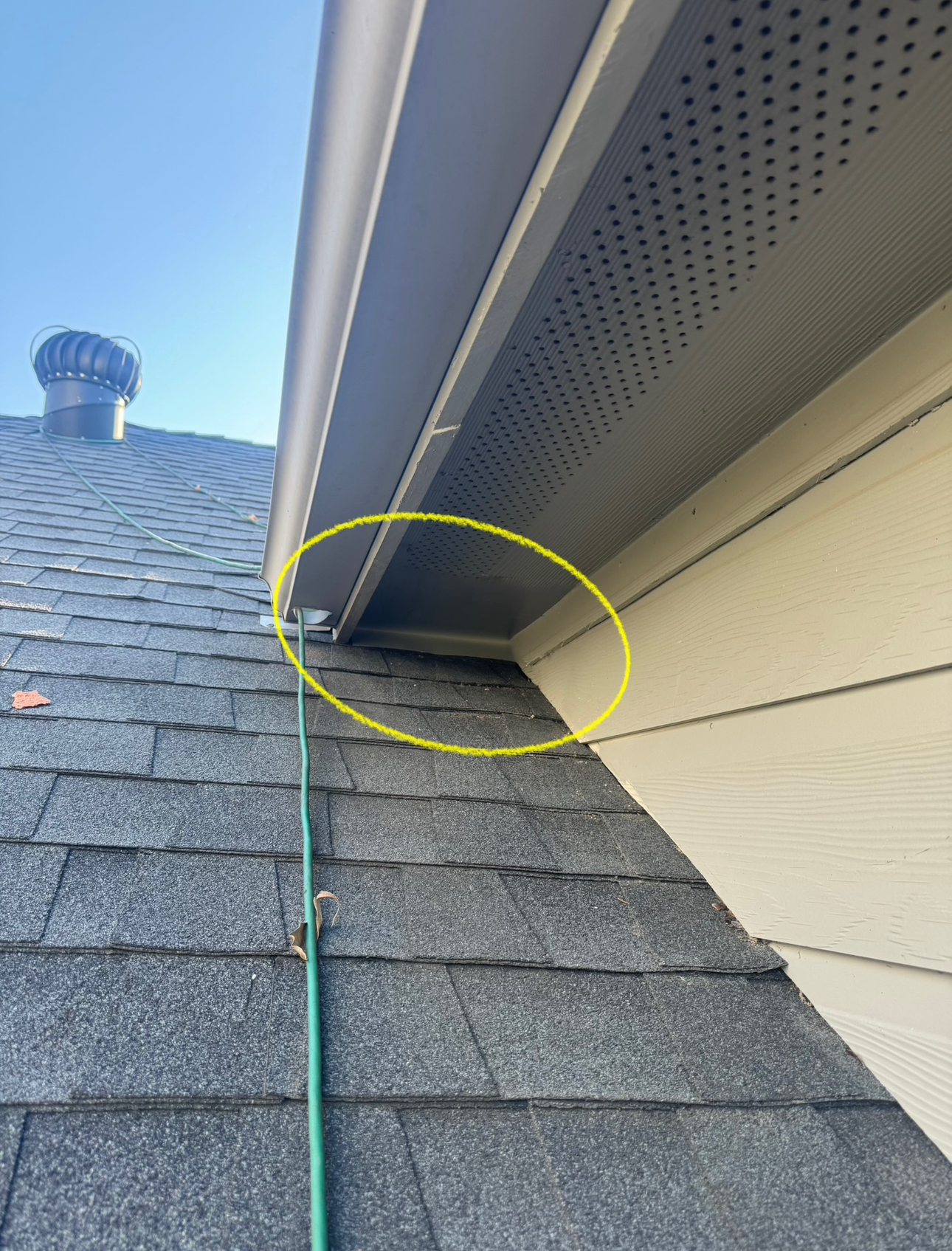 Yellow-circled area of a roof where the shingles meet the soffit, with a green hose running down.