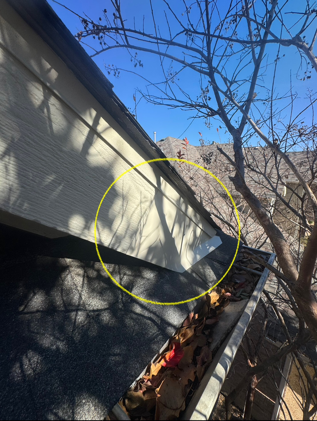 A house corner with a gutter full of leaves; a yellow circle highlights the area of the gutter.