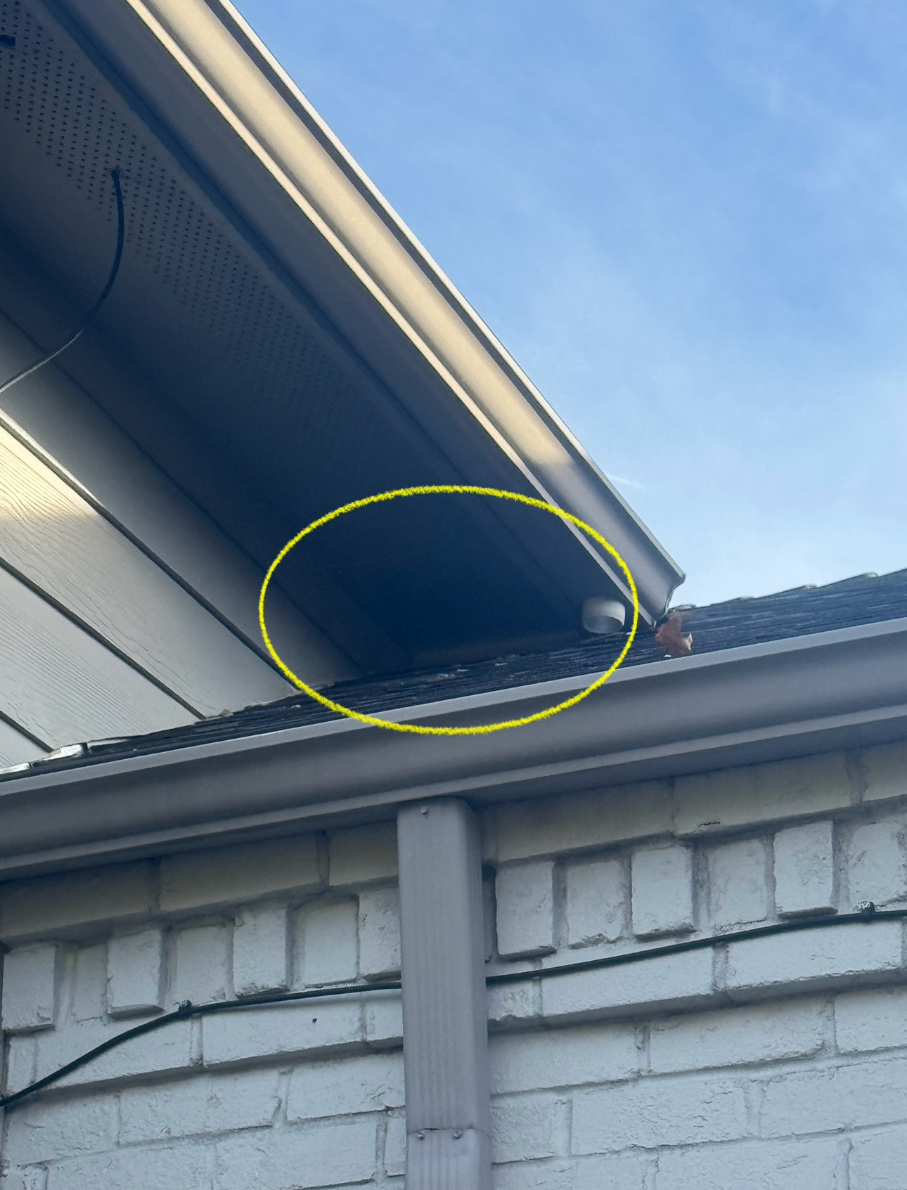 Yellow-circled open space under a roof overhang, likely soffit; next to gutter and brick wall.