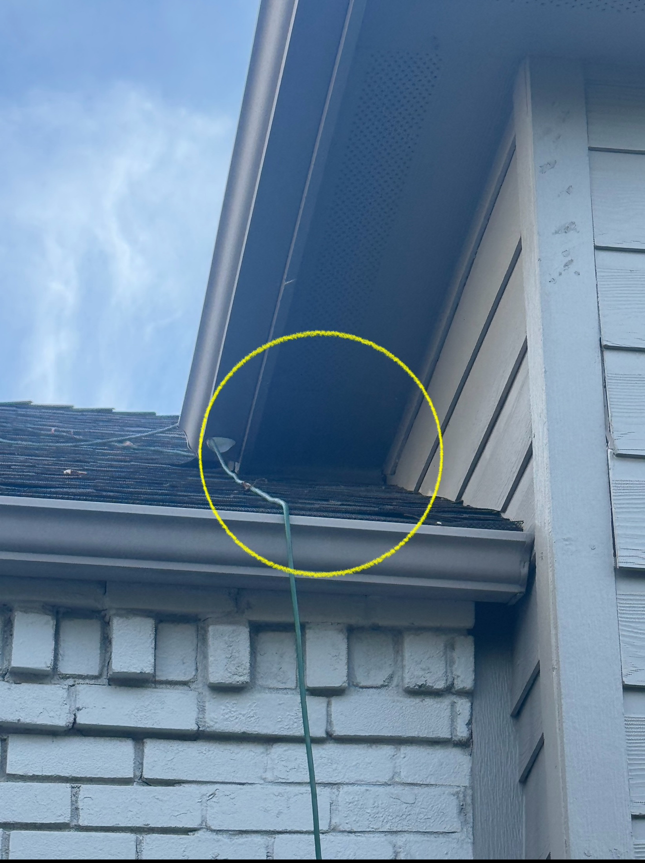 Green wire running from a roof to a gutter on a brick and siding house.