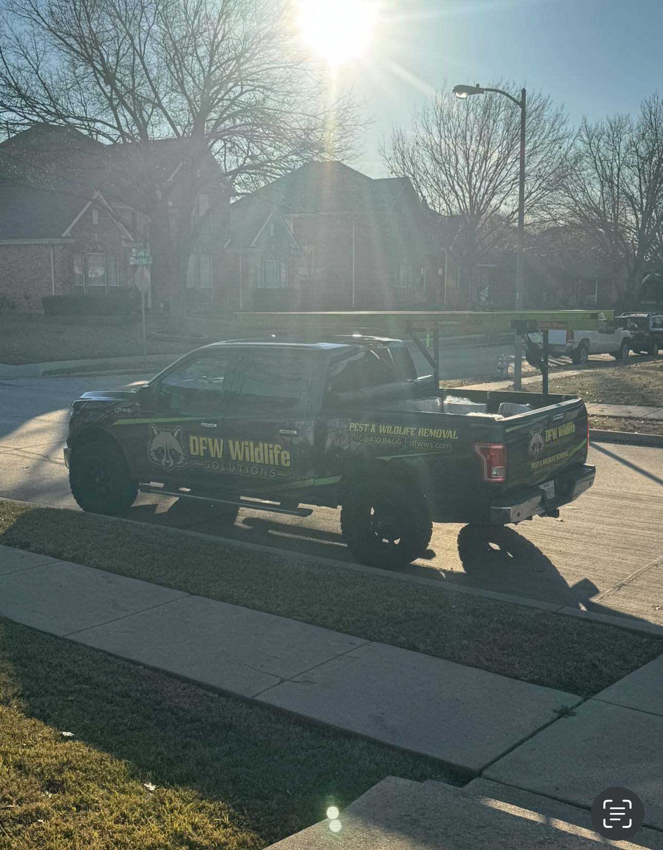 Black pickup truck parked on a residential street, displaying a pest control logo.