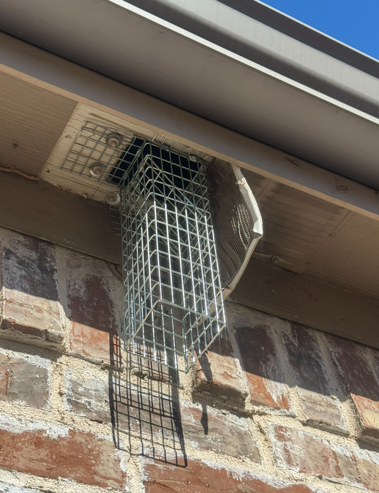 Metal cage protects a roof vent on a brick wall.