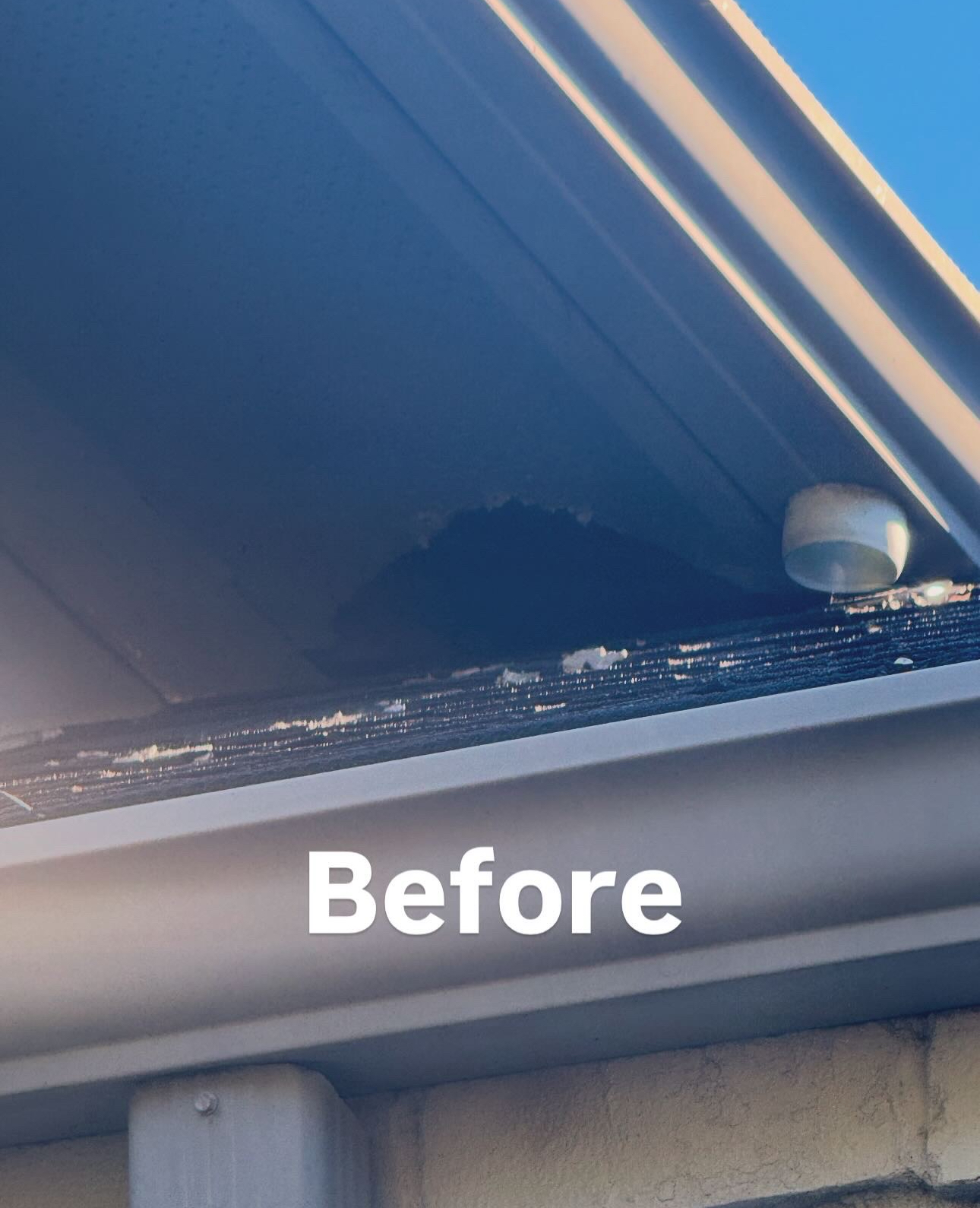 Gutter area before cleaning, showing debris and a dark stain on the underside of the eaves.