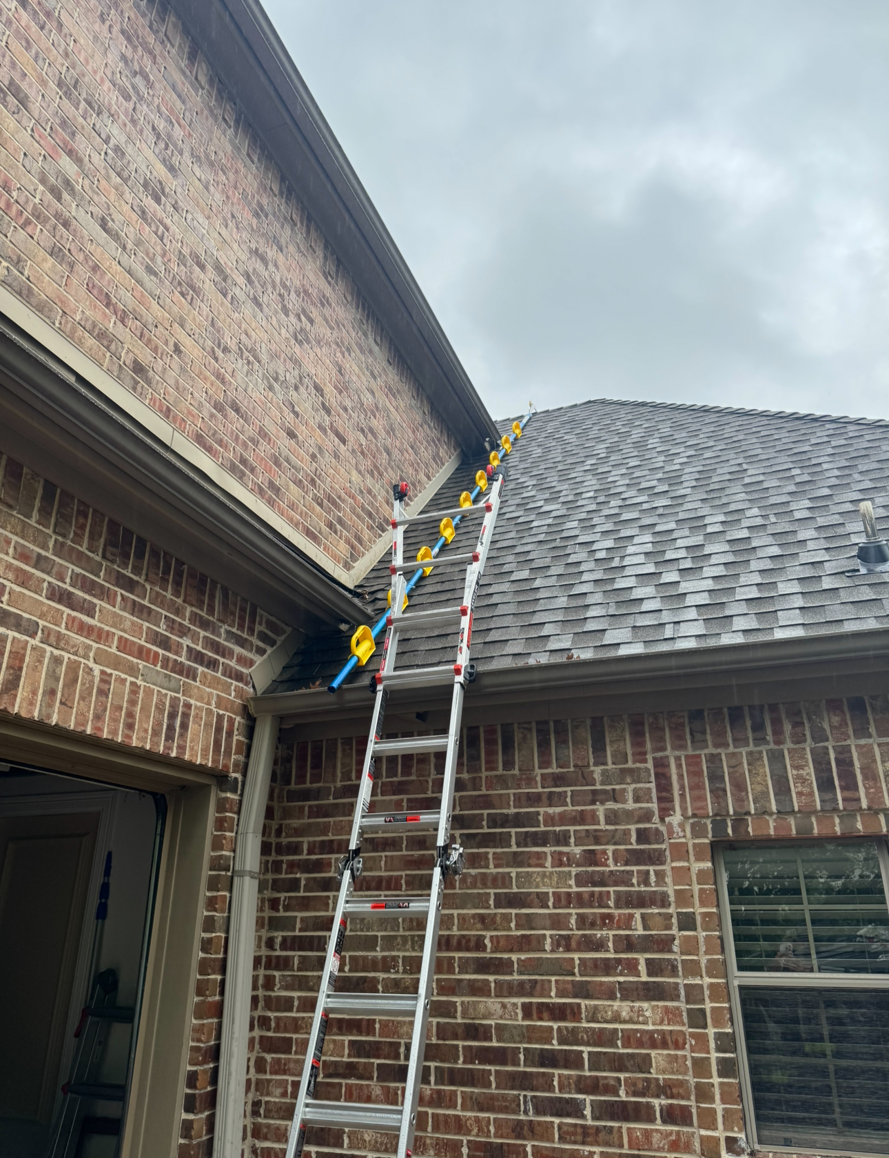 Ladder leaning against brick building, roof, yellow standoffs.