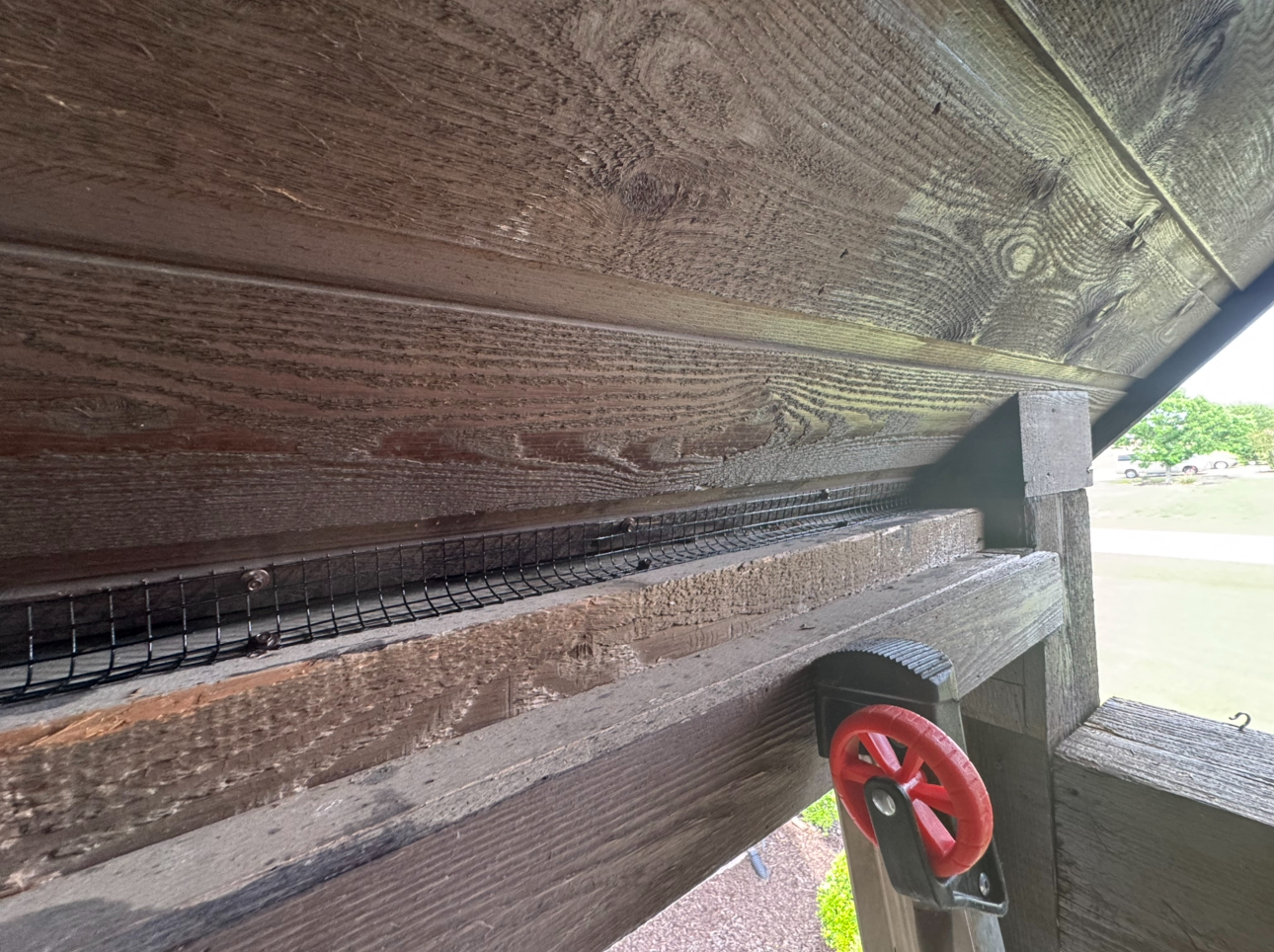 Close-up of a wooden structure with a dark brown roof and beams, featuring a red valve and wire mesh.