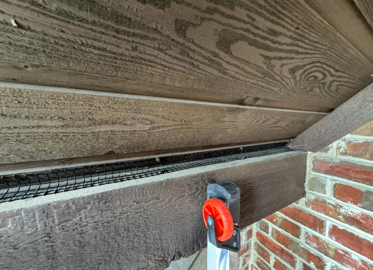 Brown soffit with installed metal mesh, next to brick. A red and black tool holder is visible.