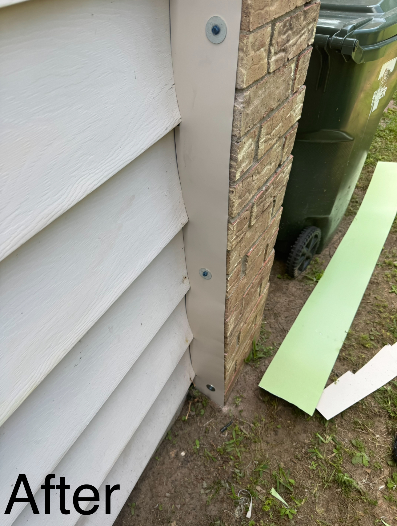 Tan siding meets faux stone column, trimmed with beige. Bolts secure the trim. Green trash bin is visible.