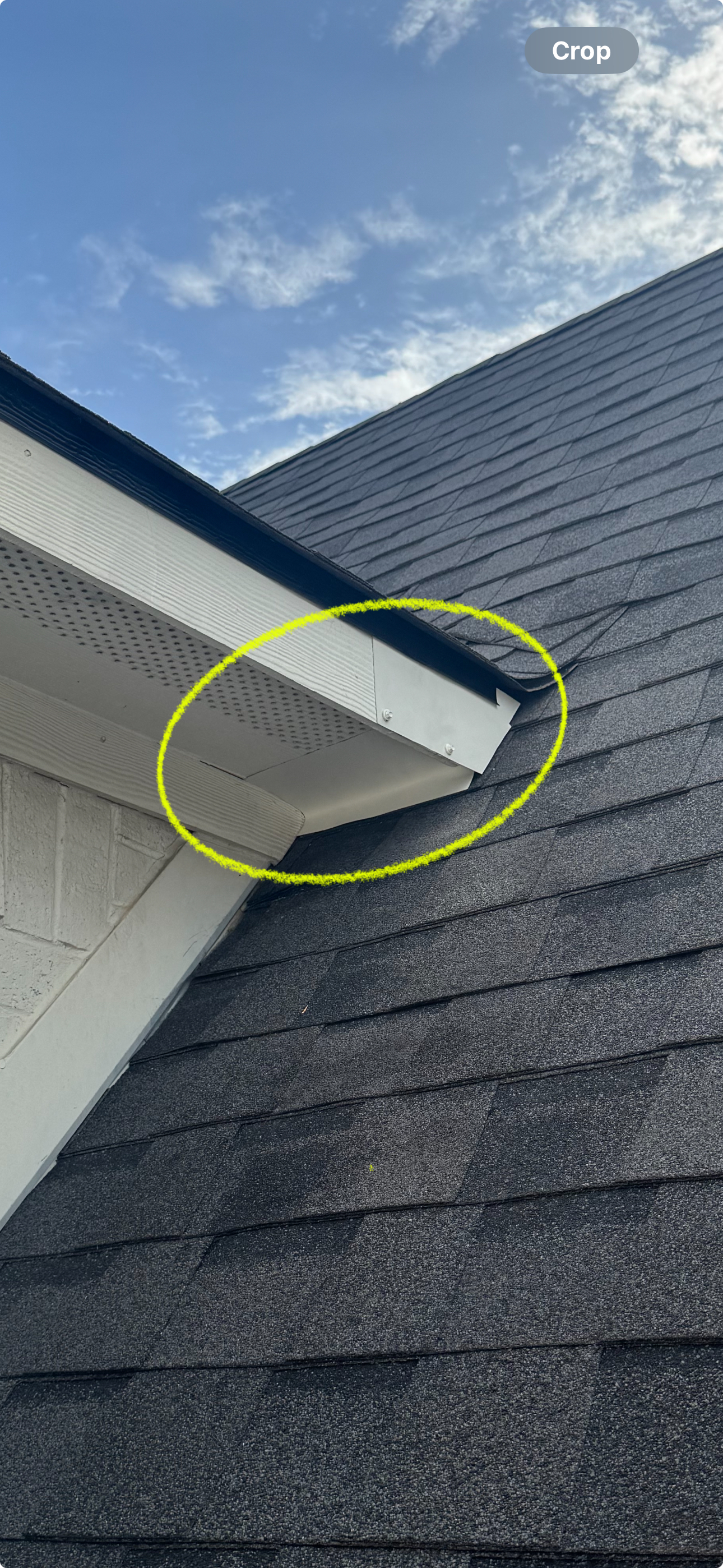 Close-up view of a roof's edge and corner of a house, with a clear blue sky in the background.