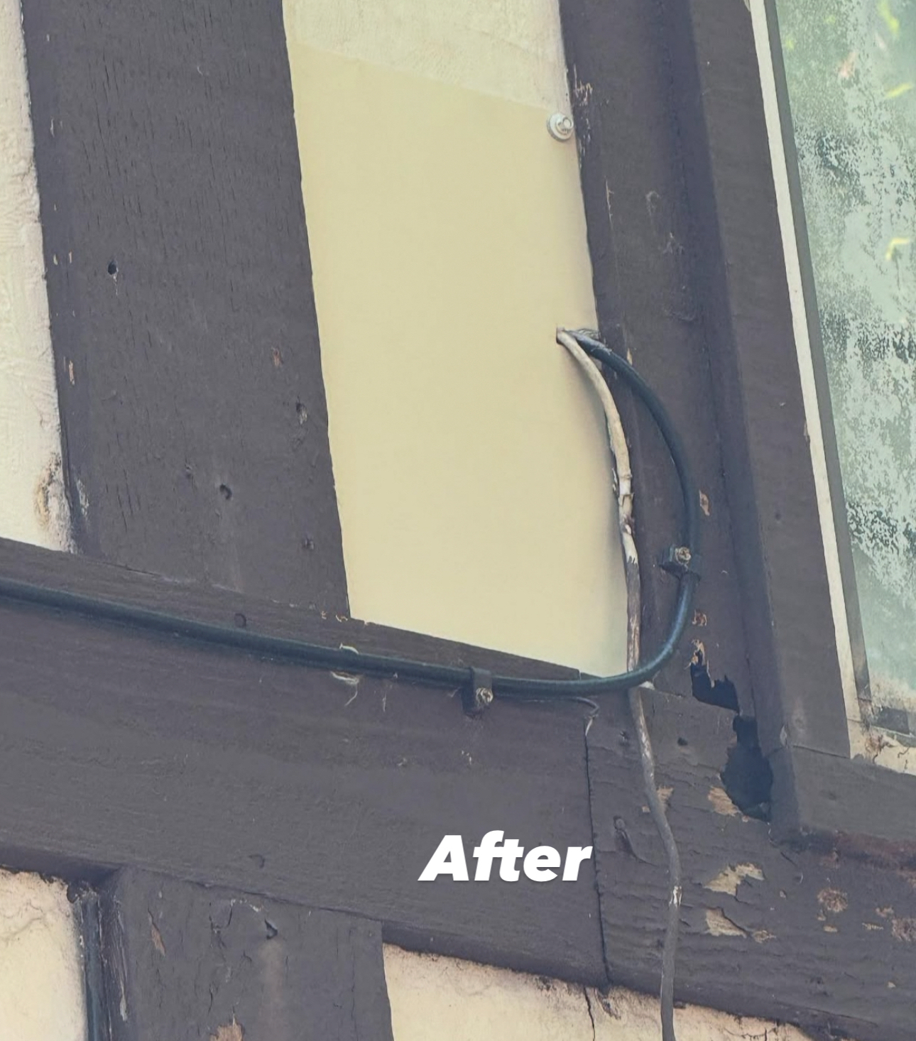 Close-up of building exterior with cream-colored siding and black trim; a black cable is attached to the siding.