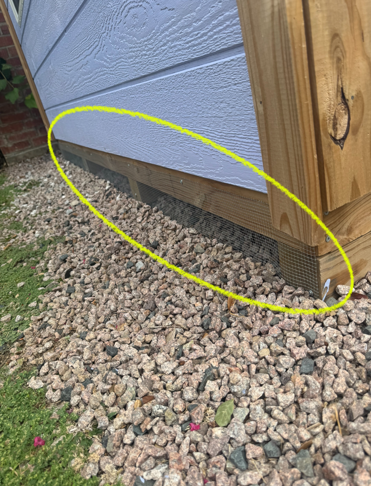 Yellow-circled shed base with wire mesh to prevent animal entry, surrounded by gravel, outdoors.