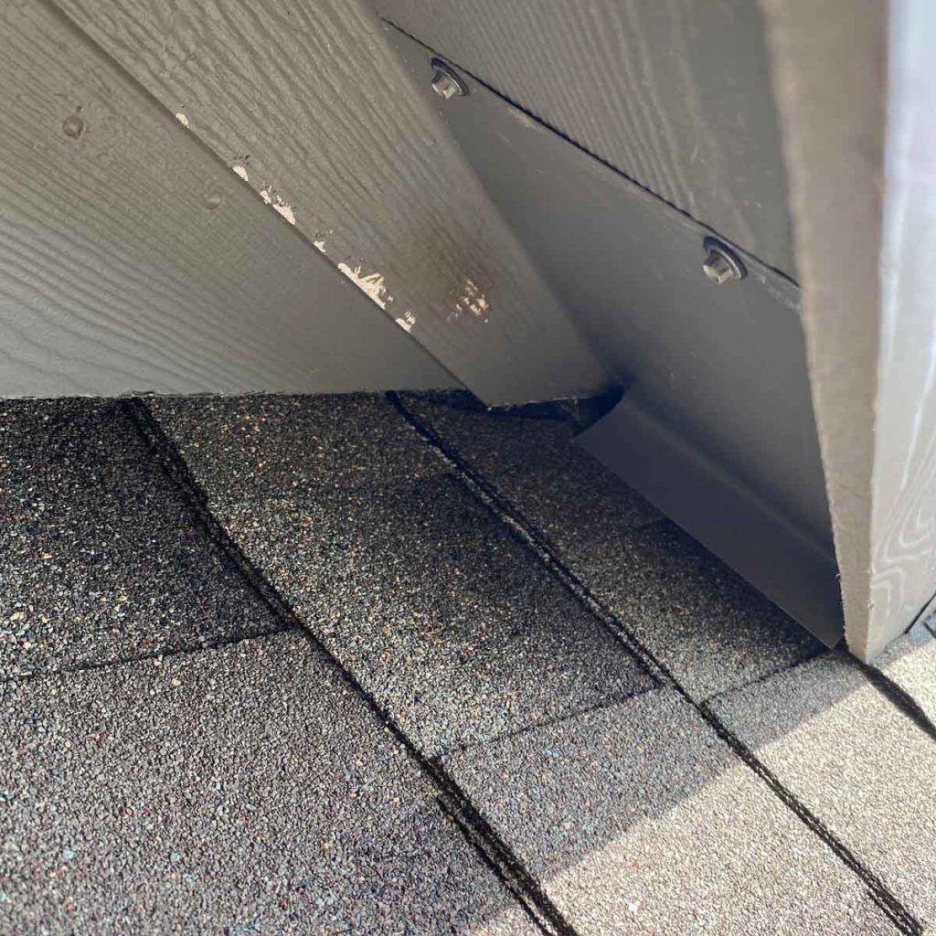 A close up of a roof with shingles and a white wall.