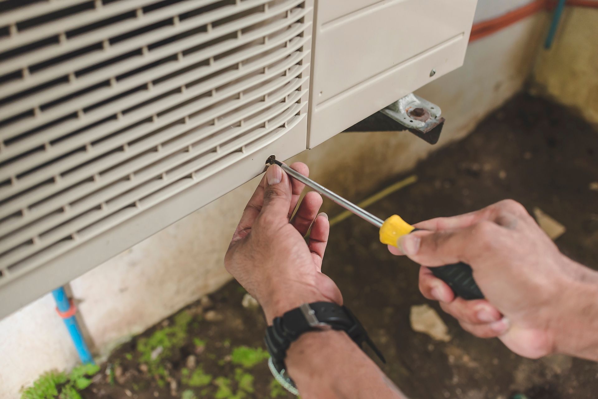 A man is fixing an air conditioner with a screwdriver.