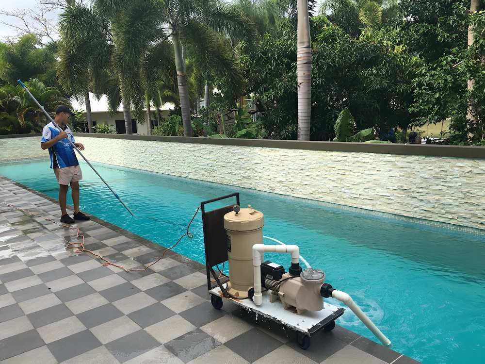 A Man is Cleaning a Swimming Pool With a Mop — Sun City Pools In Hyde Park, QLD