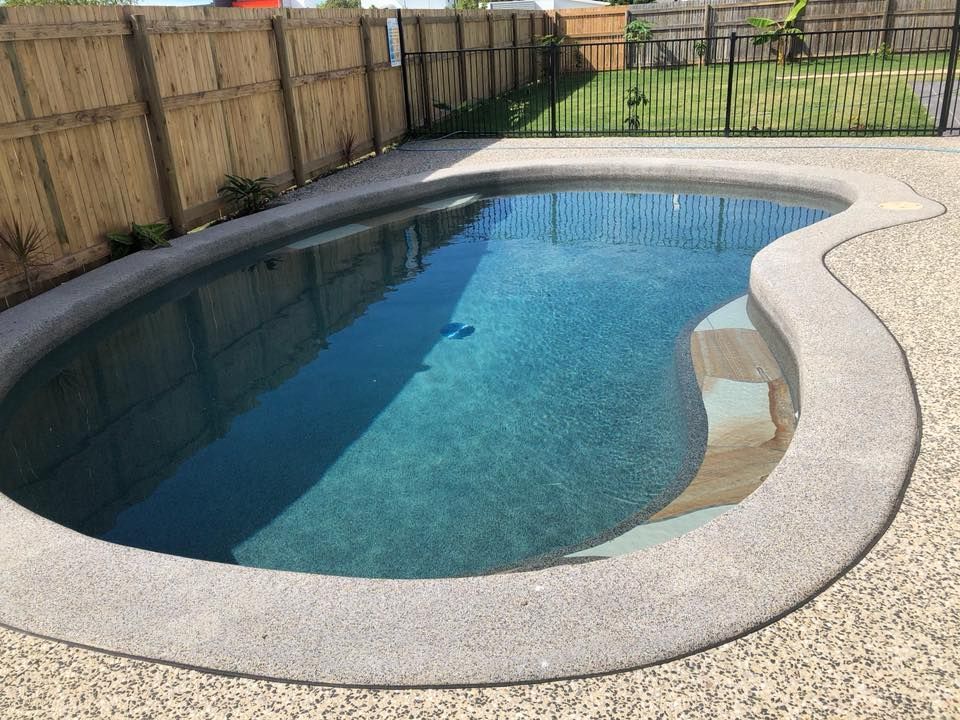 A Large Swimming Pool is Surrounded by a Wooden Fence — Sun City Pools In Hyde Park, QLD