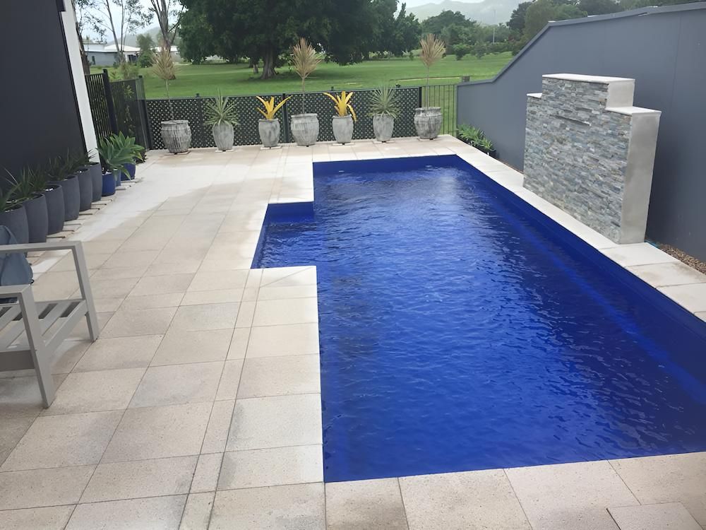 A Large Swimming Pool With Blue Water is Surrounded by Potted Plants — Sun City Pools In Hyde Park, QLD