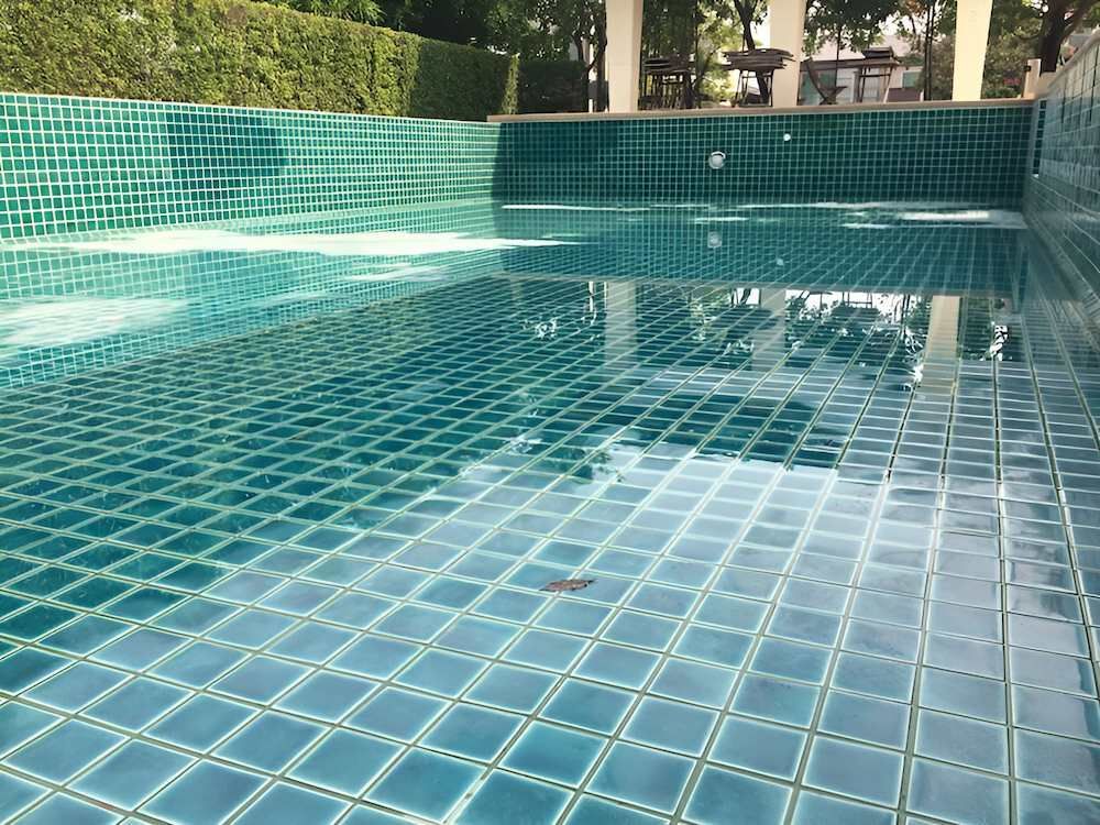 A Swimming Pool With Blue Tiles and a Reflection of Trees in the Water — Sun City Pools In Hyde Park, QLD