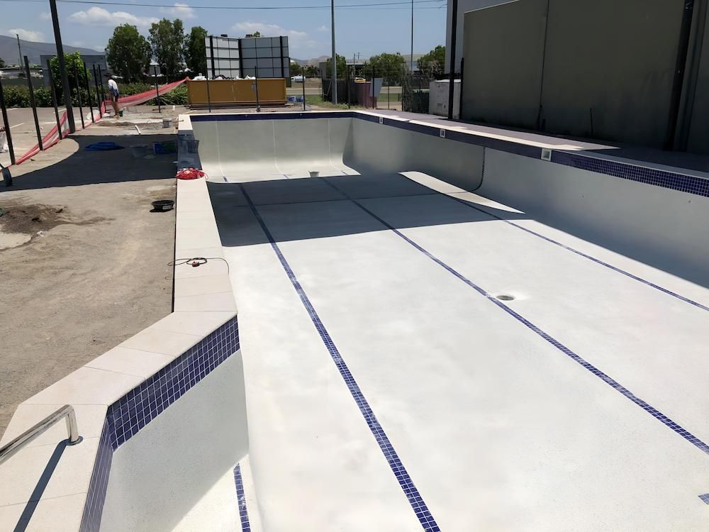 A Large White Swimming Pool With Blue Trim is Being Built — Sun City Pools In Mount Louisa, QLD