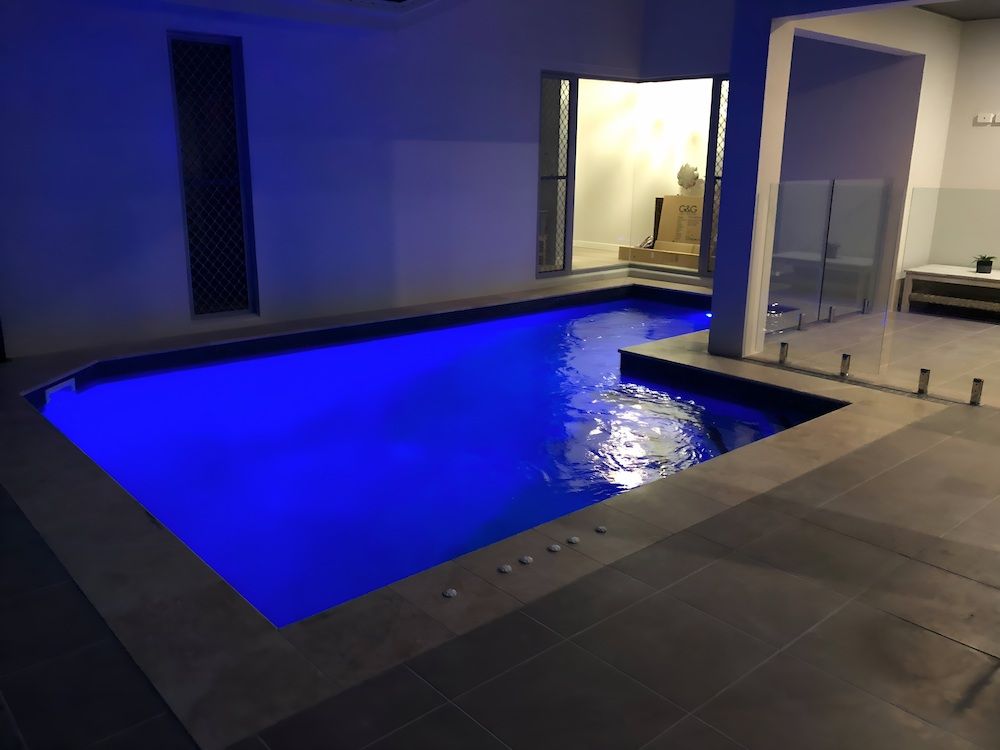 A Large Swimming Pool is Lit Up at Night With Blue Lights — Sun City Pools In Hyde Park, QLD