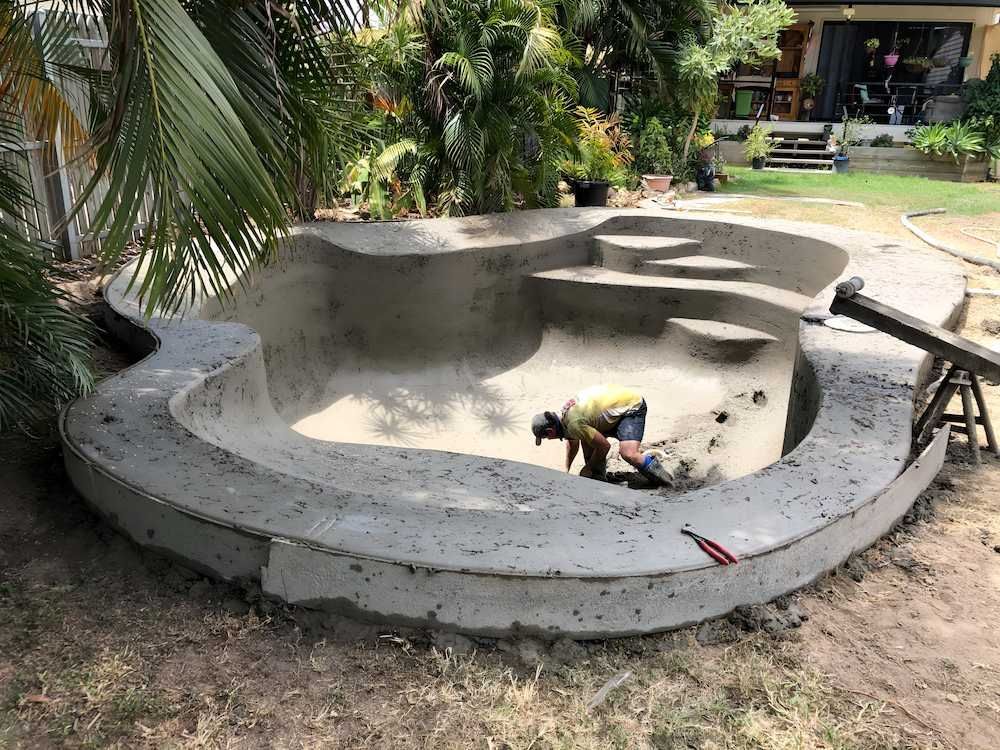 A Man is Working on a Concrete Pool in a Backyard — Sun City Pools In Bushland Beach, QLD