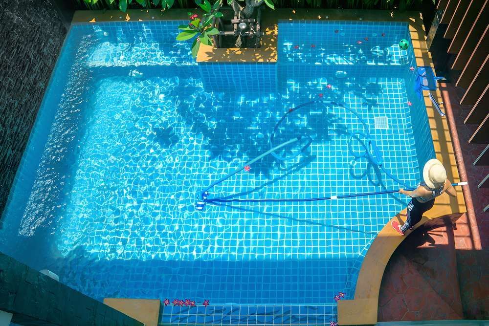 A Person is Cleaning a Swimming Pool With a Vacuum Cleaner — Sun City Pools In Hyde Park, QLD