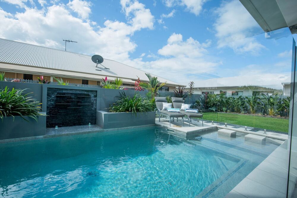 A Large Swimming Pool With a Waterfall in the Backyard of a House — Sun City Pools In Hyde Park, QLD