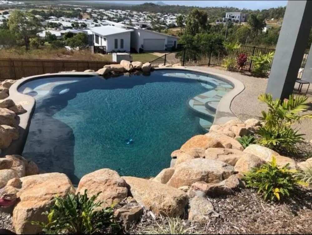 A Large Swimming Pool is Surrounded by Rocks and Plants — Sun City Pools In Hyde Park, QLD