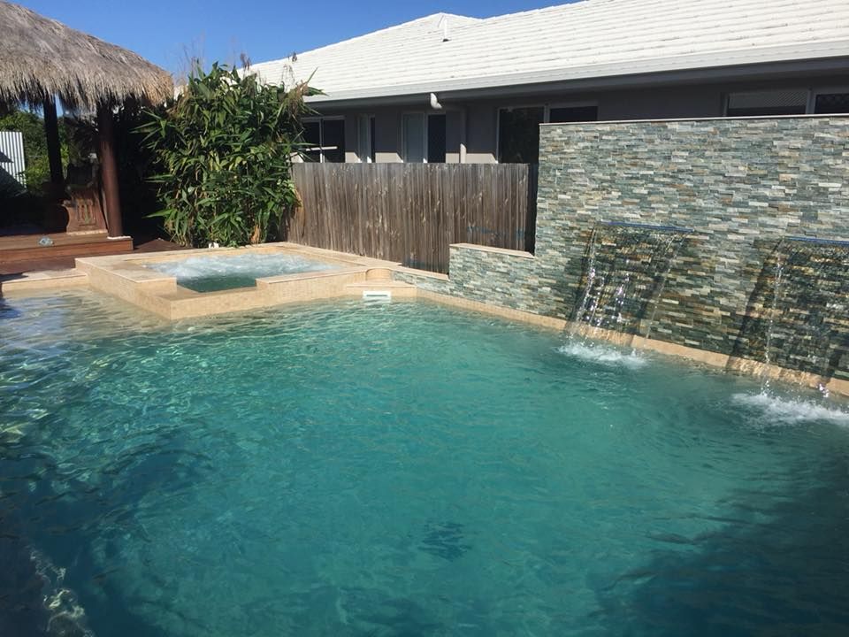 A Large Swimming Pool With a Waterfall in Front of a House — Sun City Pools In Hyde Park, QLD