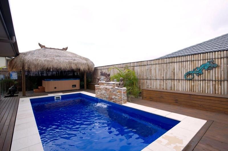 A Large Swimming Pool With a Thatched Hut in the Background — Sun City Pools In Hyde Park, QLD