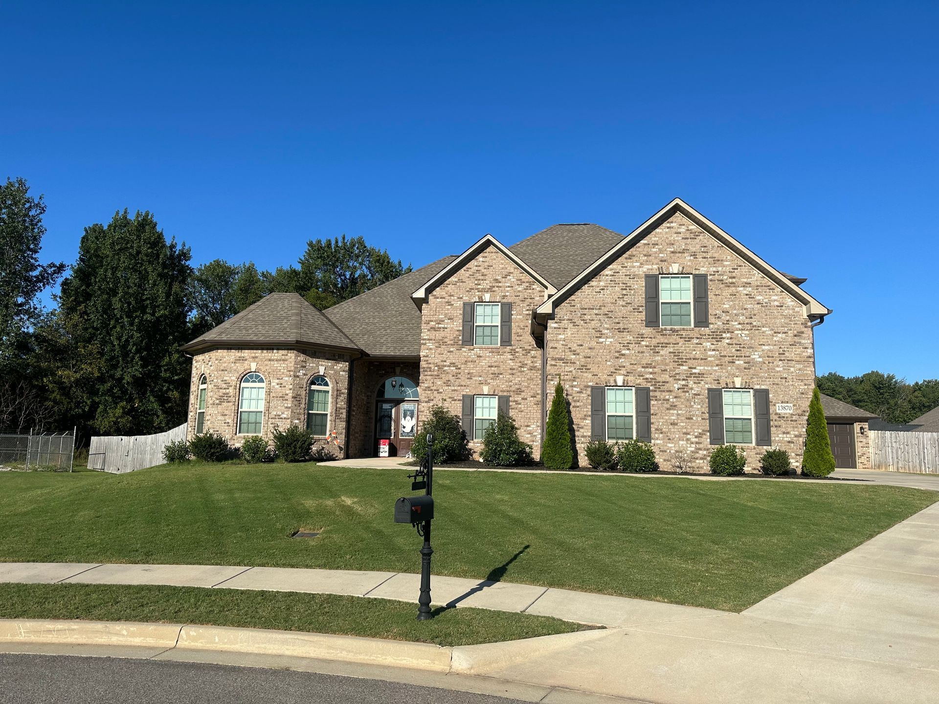 Brick house with green lawn, bushes, and a mailbox on a sunny day.