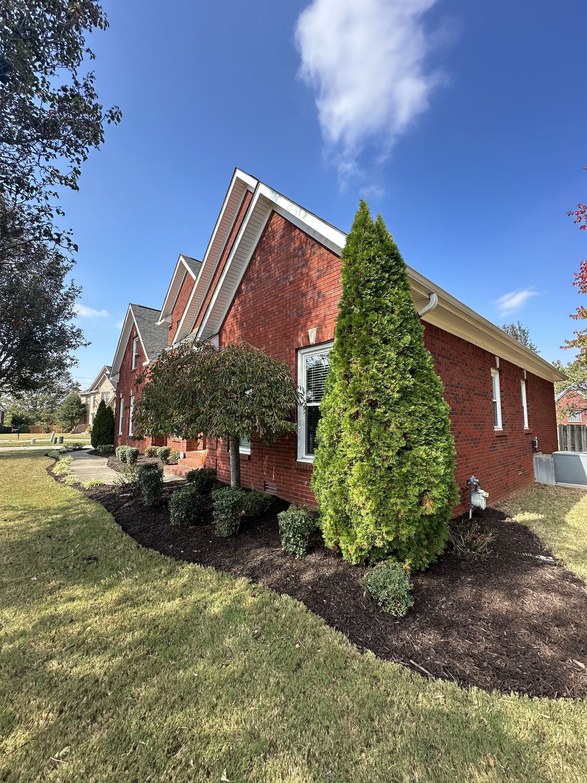 Red brick house with white trim and green landscaping under a blue sky.