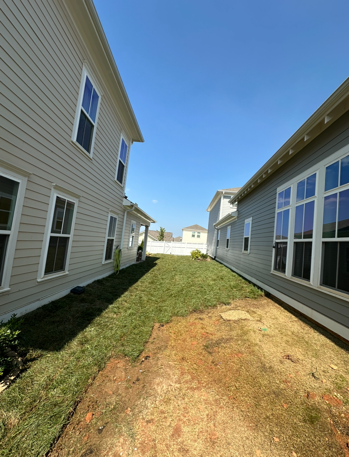 Houses with siding flank a narrow, grassy yard. Bright blue sky overhead.